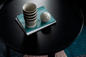 Cork Marsh's Yard. A birds-eye view of a round coffee table with a black and cream striped cup sittiong on top of a turquoise note pad. Beside it is a marble ball.