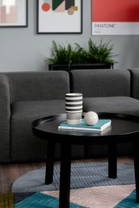 Cork's Marsh's Yard. An image of a round black coffee table in the foreground. A black and cream cup and marble ball. A grey couch in the background with art on the wall above the couch