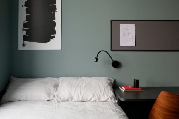 Cork Marsh's Yard. In the left foreground of the image is a double bed, highlighting the pillows. Above the bed on the wall is an art piece. To the left of the bed is a desk with a notice board above it
